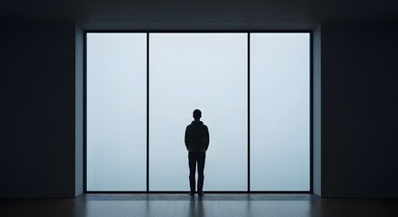 Obraz premium Silhouette of a lone man standing in a dark, minimalist room, looking out a large, bright window into the fog. This conceptual image represents solitude, contemplation, and facing the future