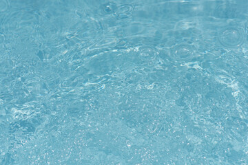 Blue water with ripples on the surface. Defocus blurred transparent blue colored clear calm water surface texture with splashes and bubbles. Water waves with shining pattern texture background.