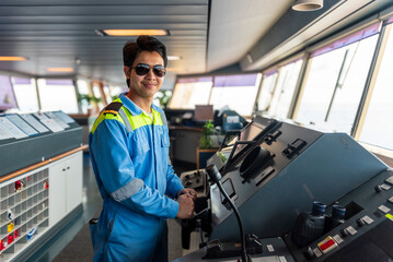 Male deck officer standing on the bridge of a merchant ship, holding the ship’s steering wheel.