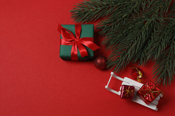 Top view of Christmas gifts with decorations and fir branches on red background
