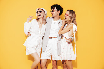Group of young three stylish friends posing in studio. Fashion man and two cute female dressed in...