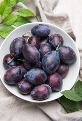 Fresh ripe plums in white bowl on table