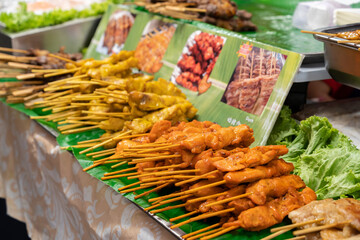 Assorted skewered grilled meat sticks display at outdoor market with fresh greens and sauces