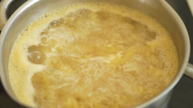 Cooking pasta in pot of boiling water on stove in kitchen. Italian Pasta. Macaroni of various varieties in very hot voda