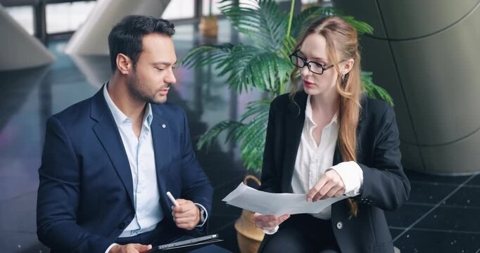 Two focused colleagues, a man and a woman, are seriously analyzing business data and reviewing documents together during a strategic planning meeting in a modern office - Powered by Adobe