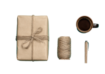 Overhead shot of a brown package, coffee mug, twine spool, & pen against black