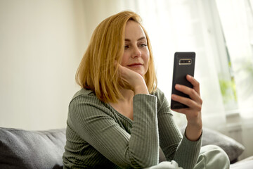 Portrait of a woman holding a smartphone and sitting on a couch © Cavan