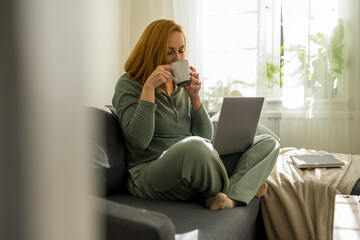 woman enjoying her coffee, while working at laptop from home © Cavan