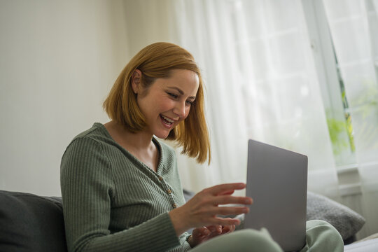 Smiling woman working on laptop at home, sitting on a couch