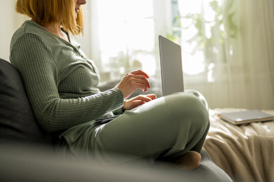 Woman working on laptop at home, sitting on a couch