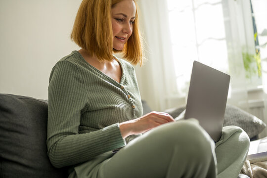 Woman working on laptop at home, typing and sitting on a couch