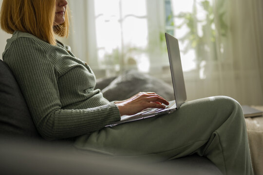 Woman working on laptop, sitting on a sofa at home
