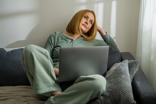 Middle age woman  working on laptop, sitting on a couch at home