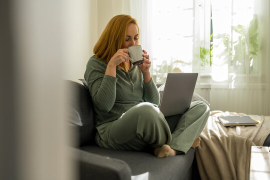 woman enjoying her coffee, while working at laptop from home