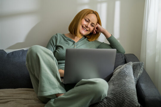 Smiling woman with laptop, sitting on a couch at home
