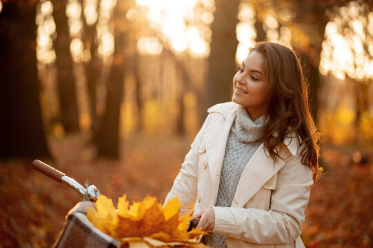 Smiling woman with a bicycle walks in the autumn forest at sunset