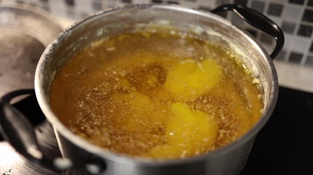 Golden ghee butter simmering in a metal pot on kitchen stove with bubbles and foam on surface showing homemade cooking process and natural clarified fat texture
