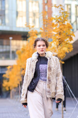 Fototapeta premium A young brunette in light warm clothes on the streets of an autumn city.