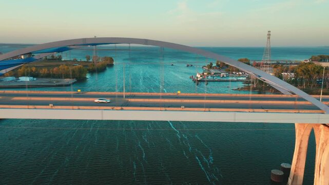 The Leo Frigo Bridge stretches gracefully over calm river waters, its blue steel arch framing boats and shoreline in the distance beneath a bright and tranquil sky.