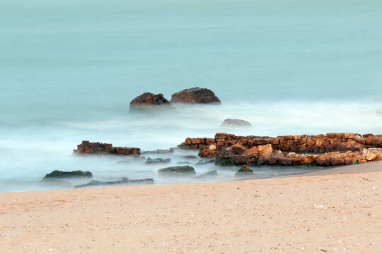 Rocky shoreline in La Marsa, Tunisia—misty waves and sandy beach captured in long exposure, evoking Mediterranean calm and natural texture.