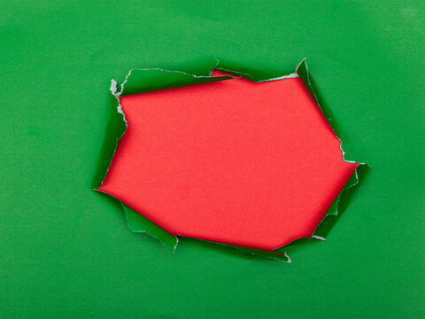 Torn hole in green paper with red background underneath.
