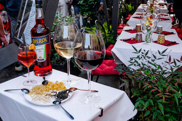 Elegant outdoor Italian restaurant table setting with Aperol bottle, glasses of red and white wine, assorted raw pasta varieties on a plate, and decorative dining setup in a Mediterranean street cafe 