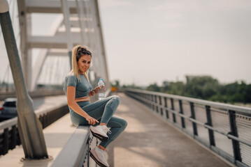 Young sporty woman drinking water on a bridge after training