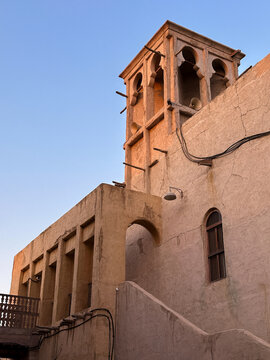 Vertical view of a preserved windtower and narrow alley in Al Seef, showcasing traditional Gulf architecture and textured facades. 