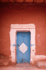 A striking blue wooden door set against a dark terracotta-red plaster wall in Morocco. color contrast, texture, and weathered surfaces classic Moroccan color palettes