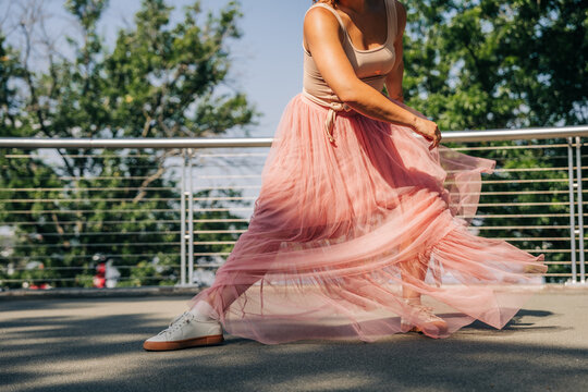 Woman dancing in pink tulle skirt outdoors on sunny day