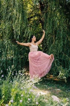 Woman dancing ballet movement under green willow tree