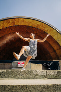 Woman dances mid-step before wooden outdoor concert shell