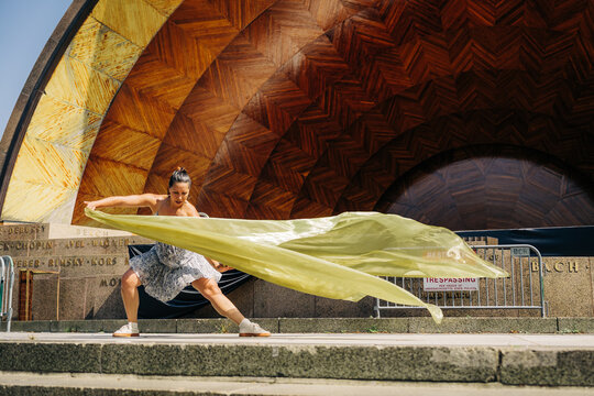 Woman dancing with fabric near outdoor bandshell stage