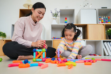 toddler girl and mother playing colorful magnetic construction toy at home
