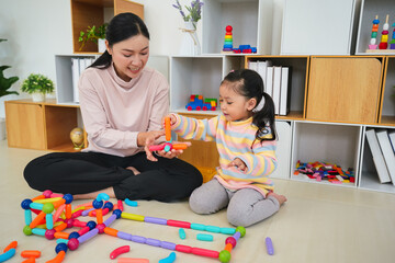 toddler girl and mother playing colorful magnetic construction toy at home