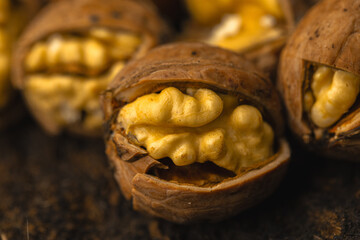 walnuts and kernels captured in a rustic natural setting. Some nuts are cracked open, revealing the rich interior texture, while others remain whole on a dark wooden surface. 
