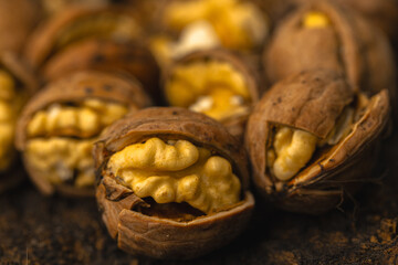 walnuts and kernels captured in a rustic natural setting. Some nuts are cracked open, revealing the rich interior texture, while others remain whole on a dark wooden surface. 
