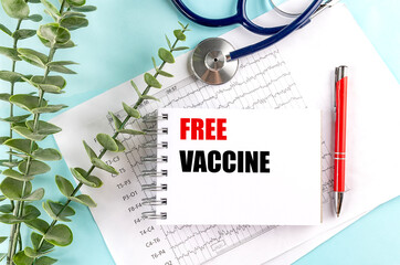 Free vaccine text on spiral notebook with red pen, stethoscope and medical charts on blue background