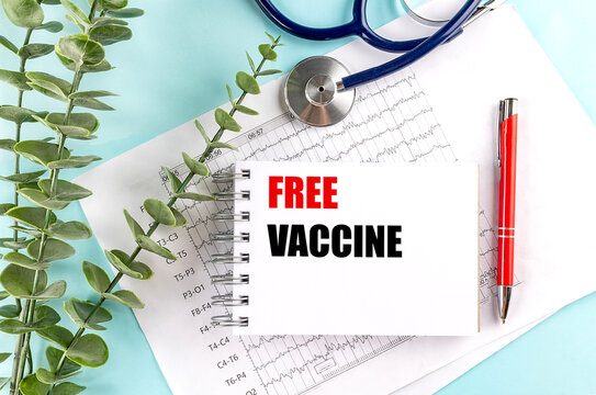Free vaccine text on spiral notebook with red pen, stethoscope and medical charts on blue background