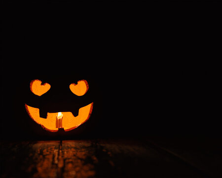 A sinister looking Halloween Pumpkin on a wooden floor with a candle burning in its mouth
