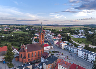Aerial views of Barwice, West Pomeranian (Zachodniopomorskie), Poland. Picturesque small town with red-brick neo-Gothic church, colorful homes, greenery, and open countryside on a summer afternoon