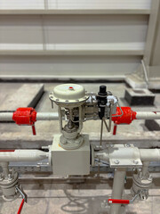 Close-up of an industrial pneumatic control valve system with connected pipes and fittings. The mechanical setup is indoors, with metallic components and precision engineering visible.