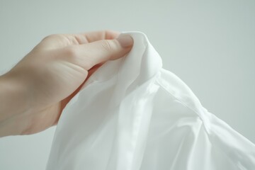 Fototapeta premium Hand Holding White Fabric: A close-up shot capturing a delicate hand gently holding a piece of pristine white fabric, highlighting texture and purity.