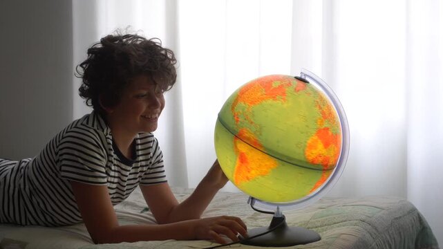 11 year old boy at home in his room looking at the globe and dreaming about where to go on his next trip to learn the geography he studied at school - desire to travel around the world 