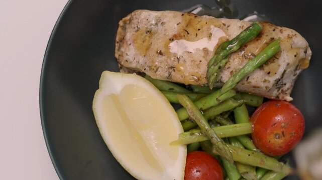 Close-up, Red Snapper Steak, Asparagus, and Tomatoes on Black plate, topped with yuzu dressing.