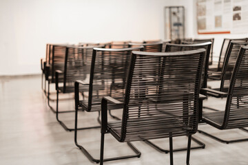 Several sleek black chairs are neatly arranged in rows within a bright gallery space. The walls feature informational displays, creating a welcoming atmosphere for visitors