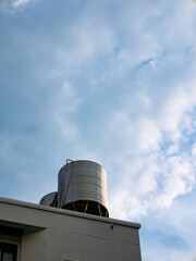 Stainless steel water storage tanks on building rooftop against blue cloudy sky - Industrial water supply system architecture