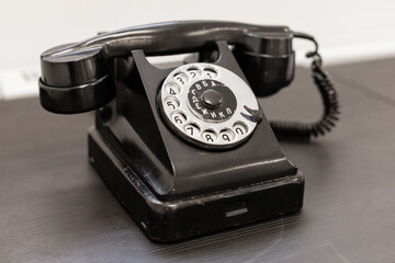 A classic black rotary telephone sits on a smooth wooden table. The design showcases circular dial numbers and a coiled cord, adding a nostalgic feel to the modern space