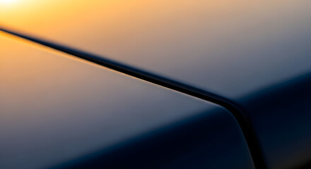 An abstract close-up of the sleek curves and lines of a dark car's bodywork reflecting a warm golden sunset