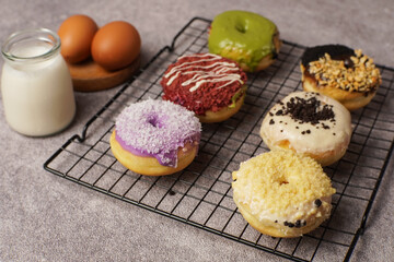 Assorted colorful donuts on a cooling rack with milk and eggs nearby, symbolizing sweet temptation faced by a child forbidden to eat them.